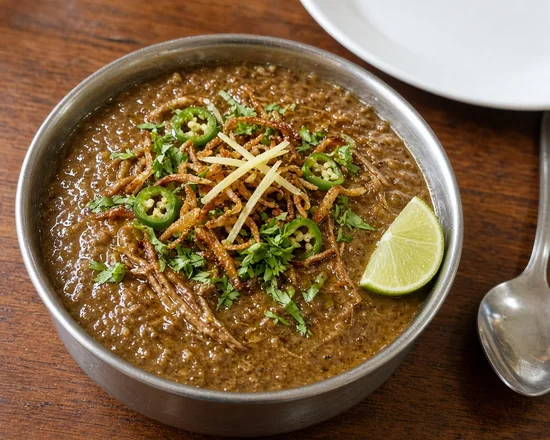 Bowl of haleem topped with crispy fried onions, ginger strips, green chilies, coriander and a lime wedge